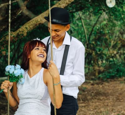 a man in a white shirt rides a woman in a white dress on a swing, the woman has a bouquet of white flowers in her hands, they smile