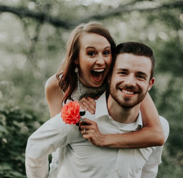man and woman laugh, woman is on the man's back and hold a flower